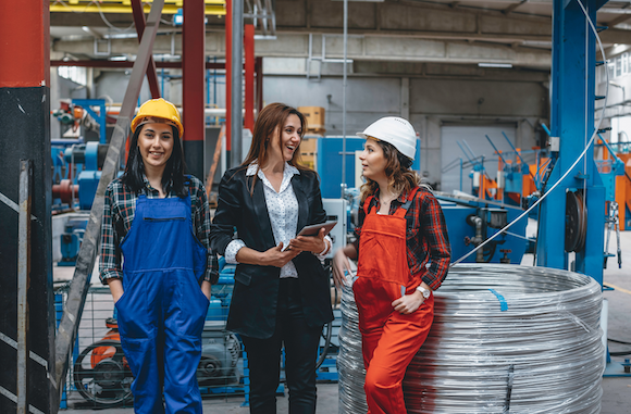 three female employees interacting on the job, one in a suit and the other two in hard hats, all smiling because employee experience is high and they enjoy the internal communications and HR processes within their company